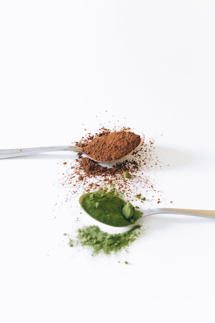 Brown and green powders on spoons against a white background.